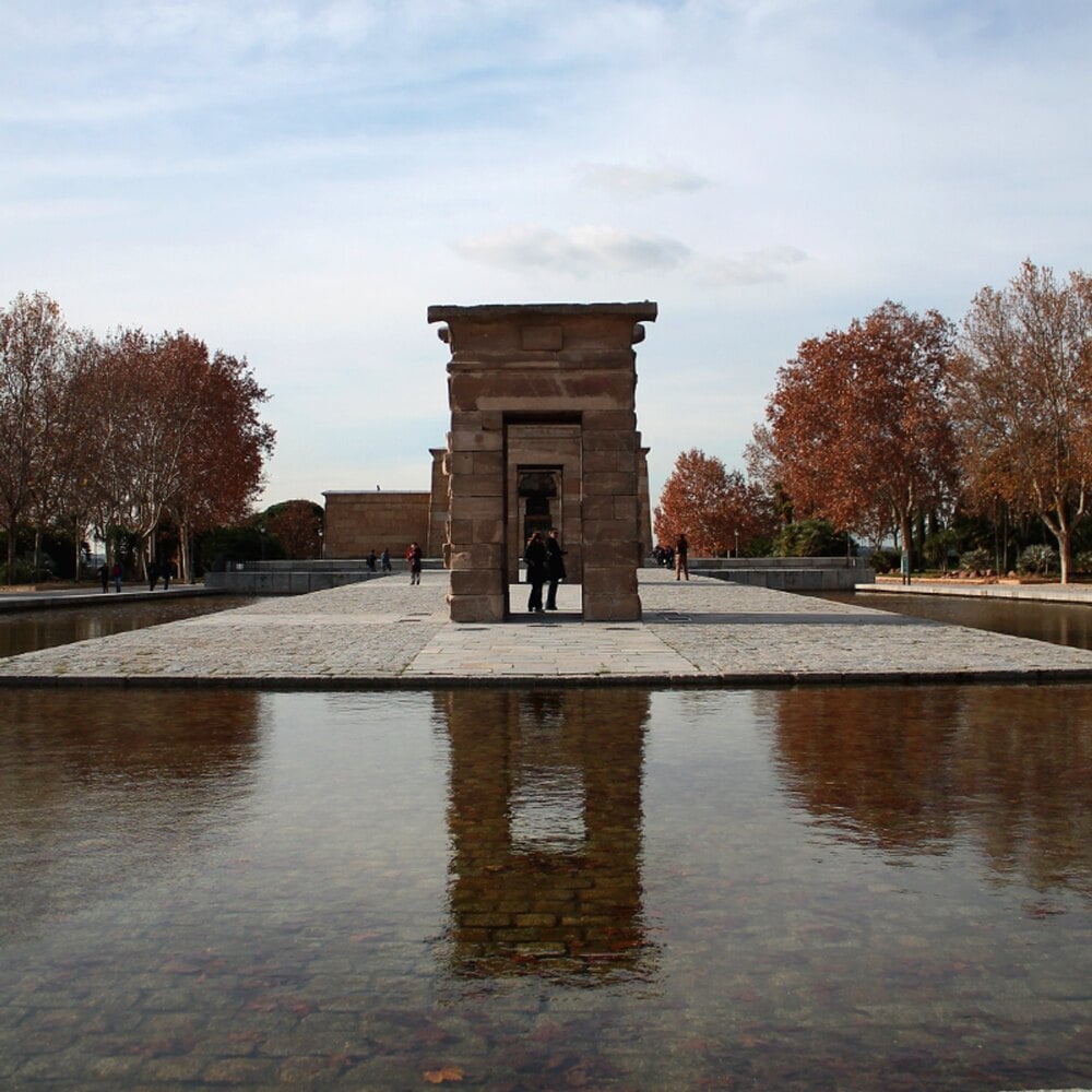 The Temple of Debod in Madrid, showing the stone structure reflected in a surrounding pool of water.