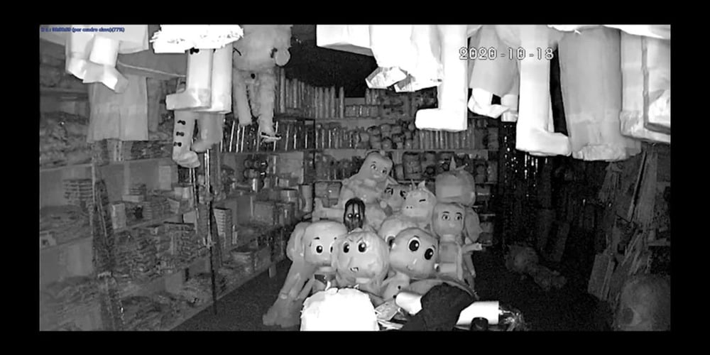 Black and white security camera footage of a store shelves filled with various cartoon character mascot heads and stuffed figures.