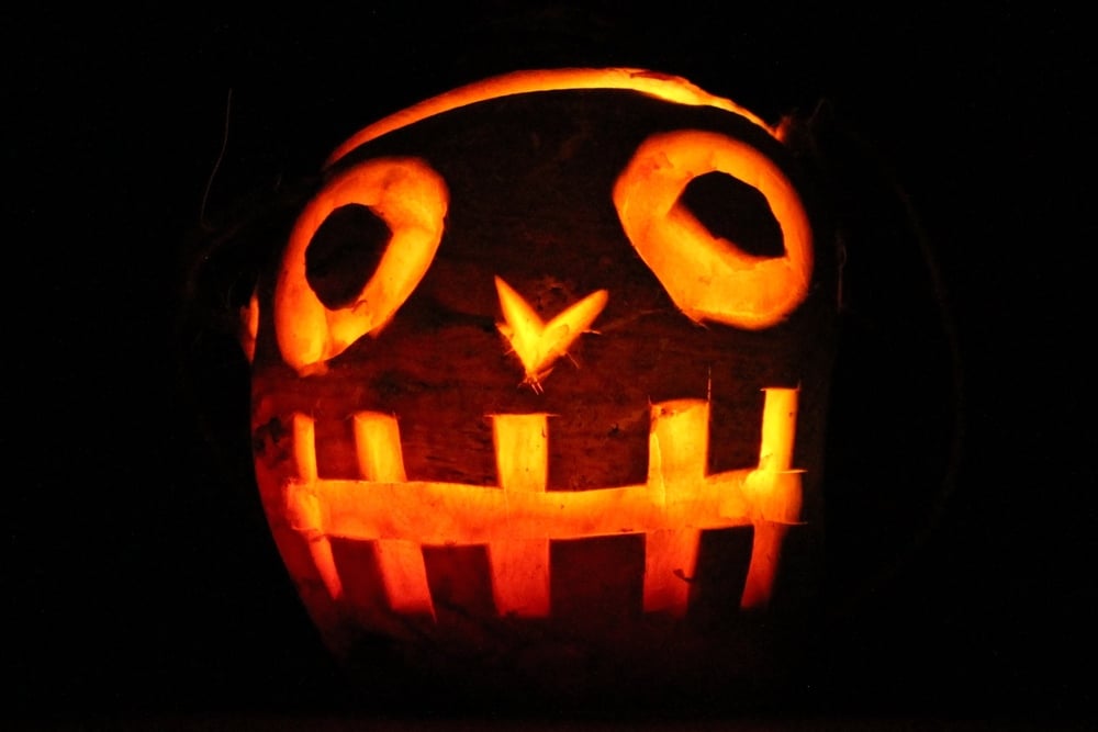 A carved pumpkin with a glowing, mischievous face against a black background.