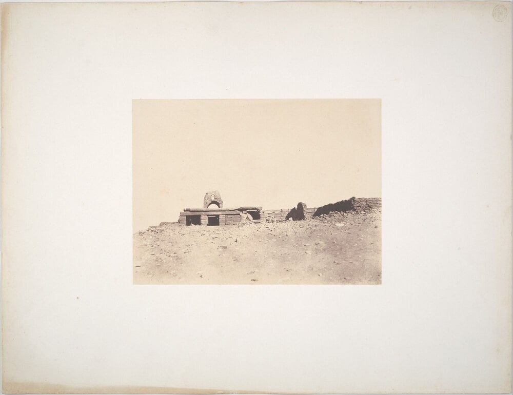 Sepia-toned photograph of ancient stone ruins perched on a barren, sandy hill.