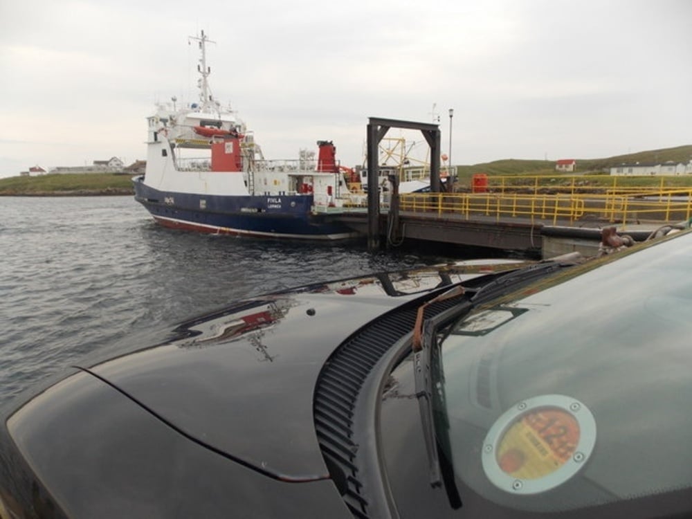 A ferry docked at a pier, viewed from the driver’s seat of a car.