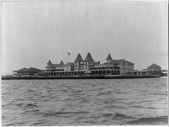 Large multi-story waterfront hotel with many gables and towers, viewed from the water.