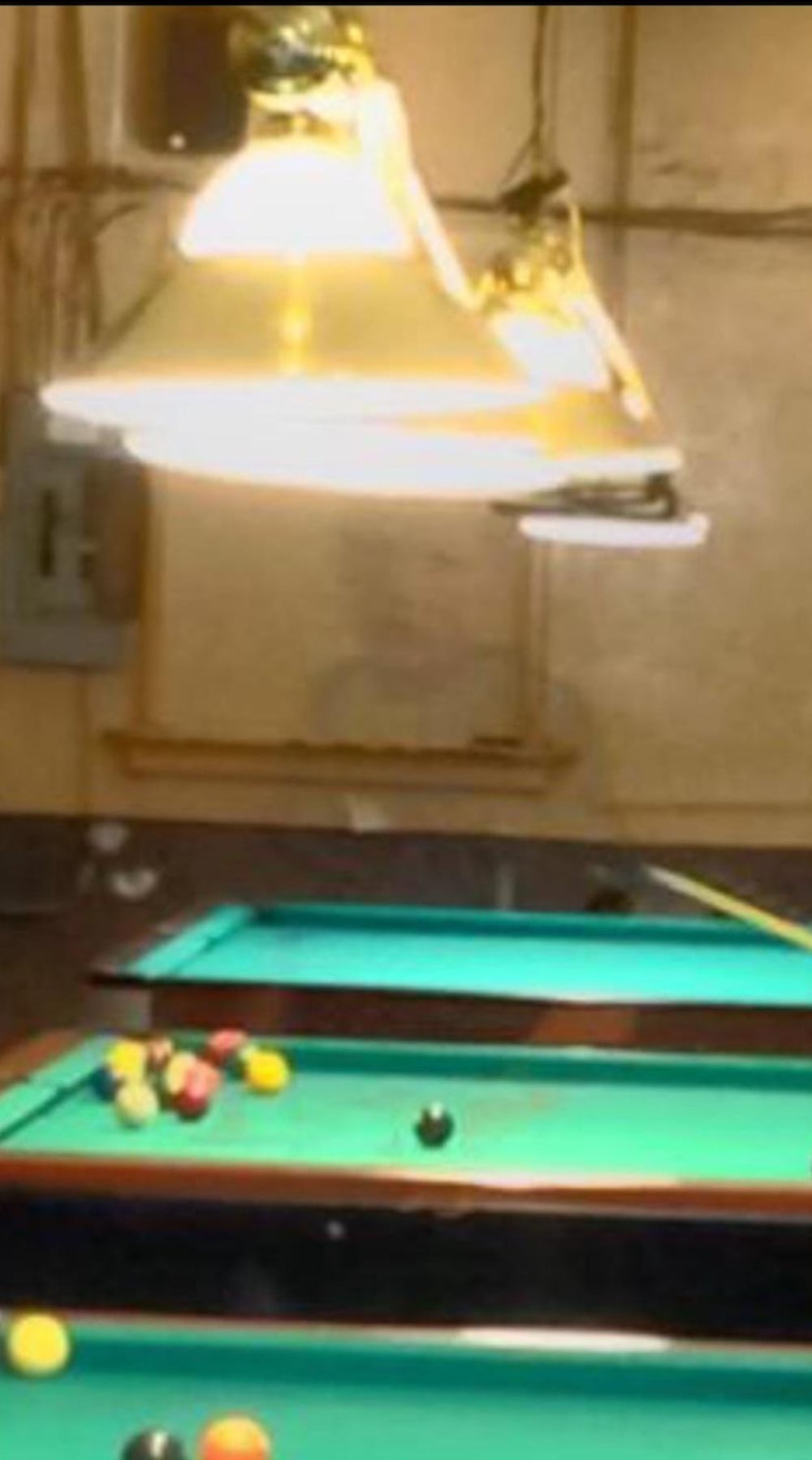 Two pool tables in a dimly lit room under hanging lamps.