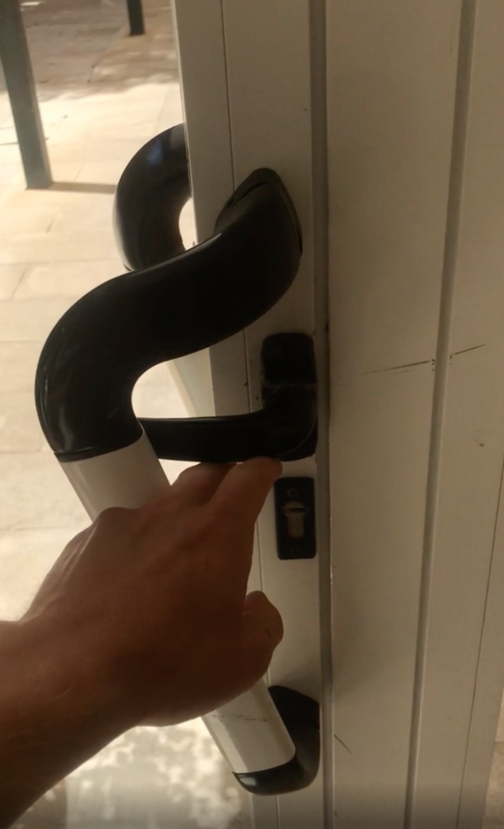 A hand pushes down on the black handle of a white door.