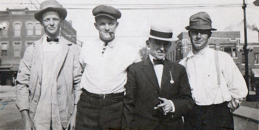 Four men in early 20th-century attire standing on a city street.