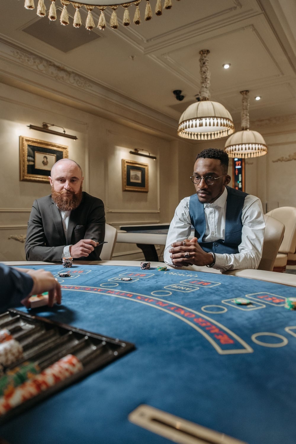 Two men sit across from each other at a blue casino table during a card game.