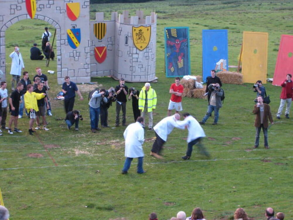 Two people in costumes perform shin-kicking on a grassy field.