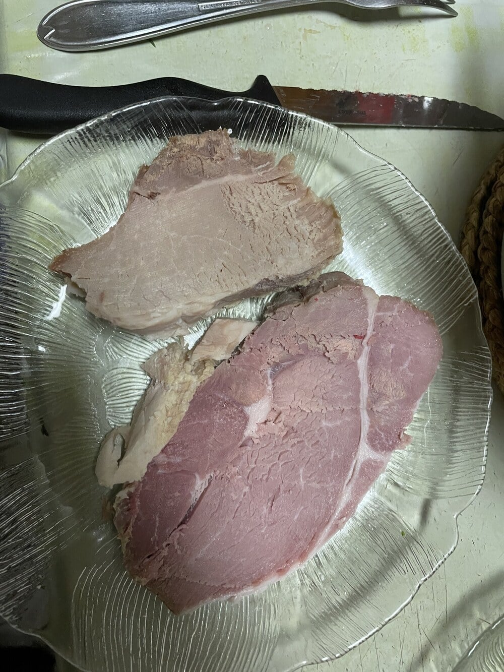 Two slices of cooked ham on a clear glass plate with a knife and fork nearby.