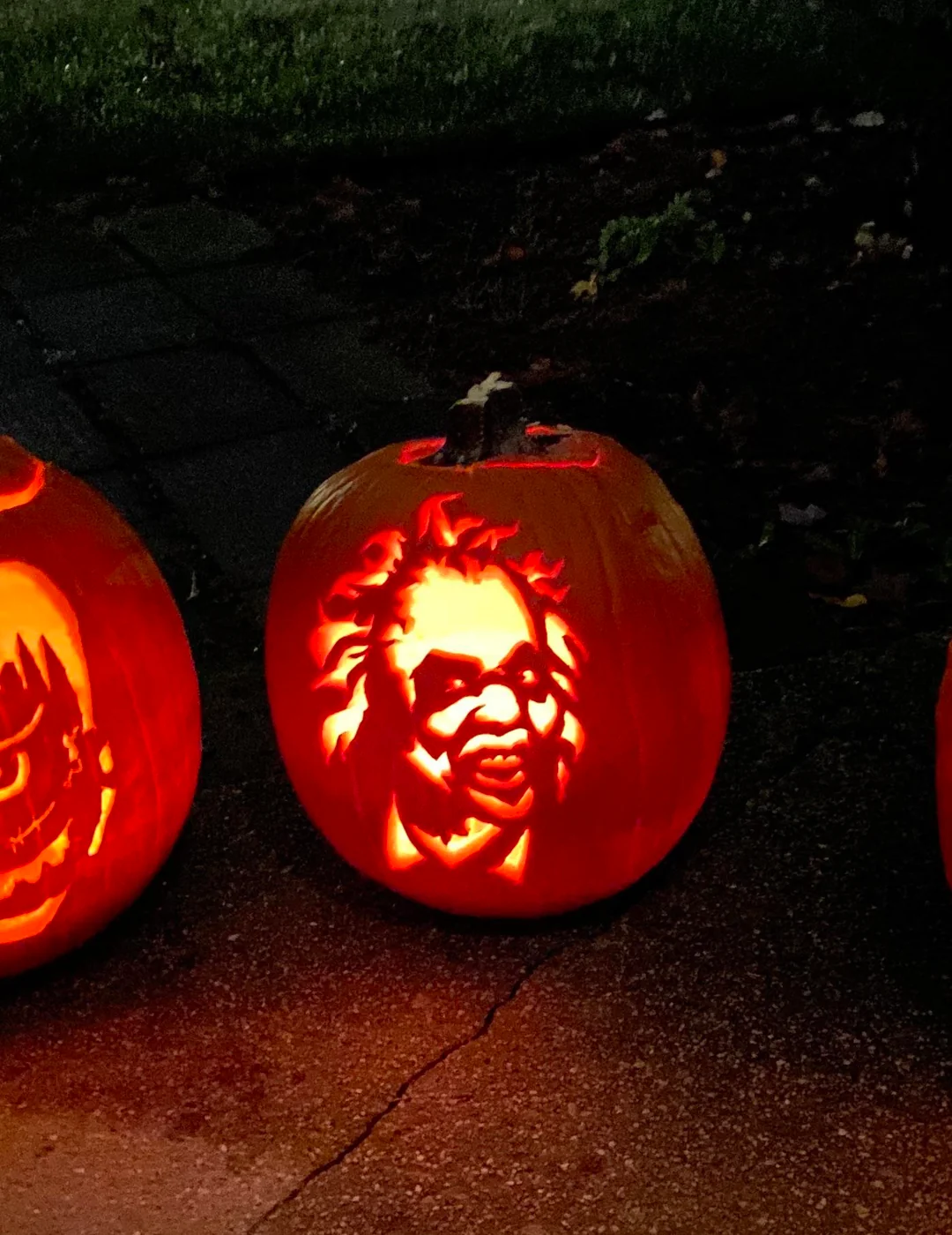 A jack-o’-lantern carved with the face of Beetlejuice glowing at night.