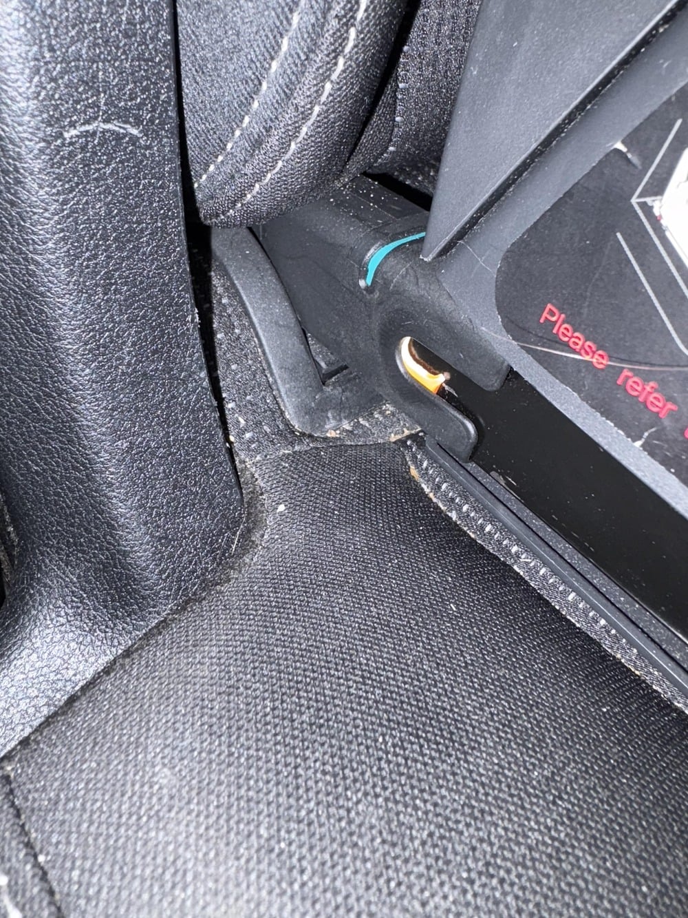 A child safety seat base latched into a vehicle seat anchor, showing a green indicator tab.