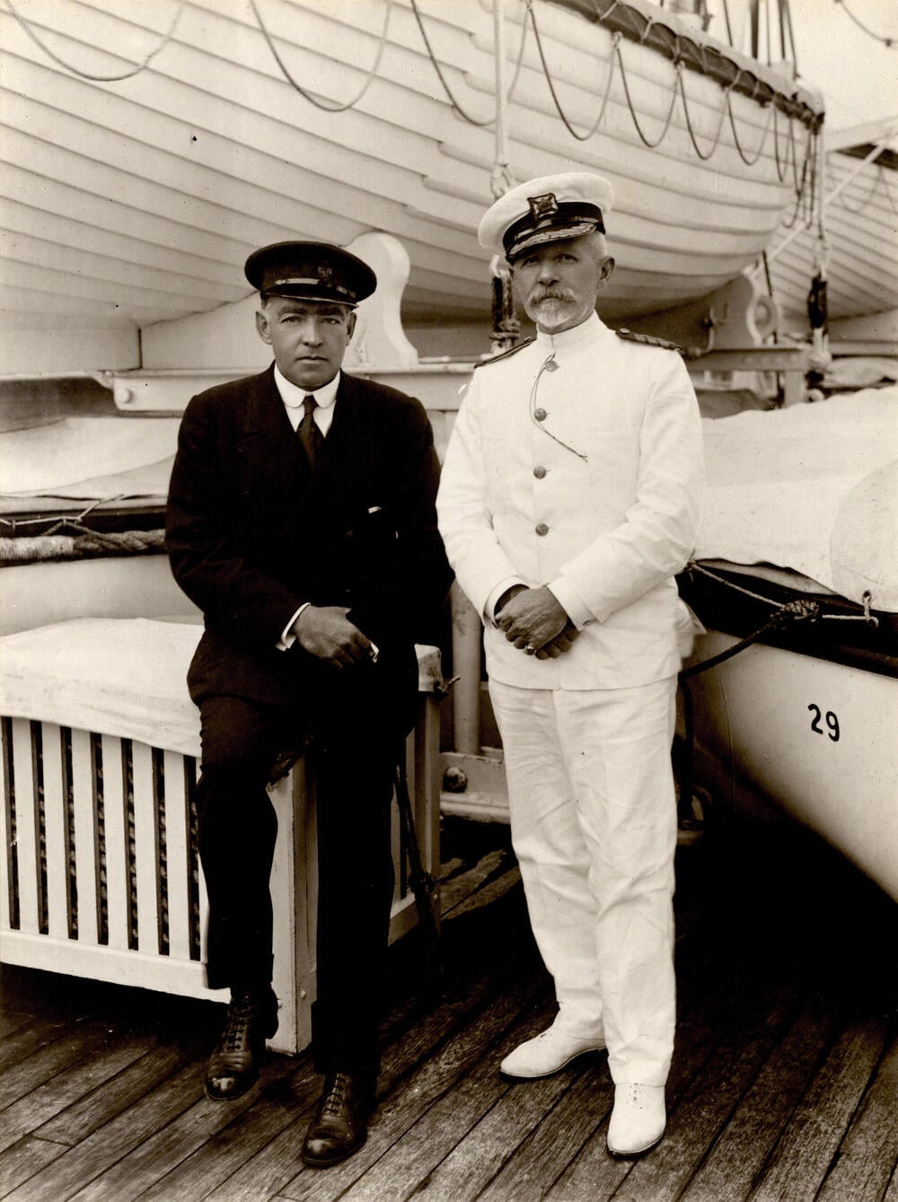 Two men aboard a ship, including an officer in white uniform beside a lifeboat marked 29.
