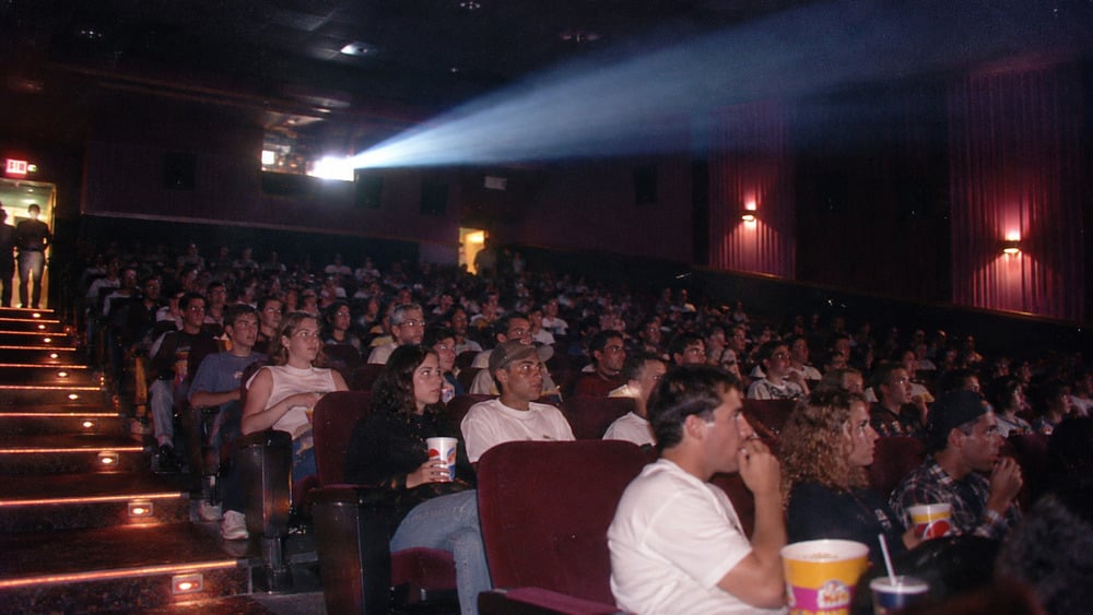 A crowded movie theater auditorium with a visible projector beam shining toward the screen.