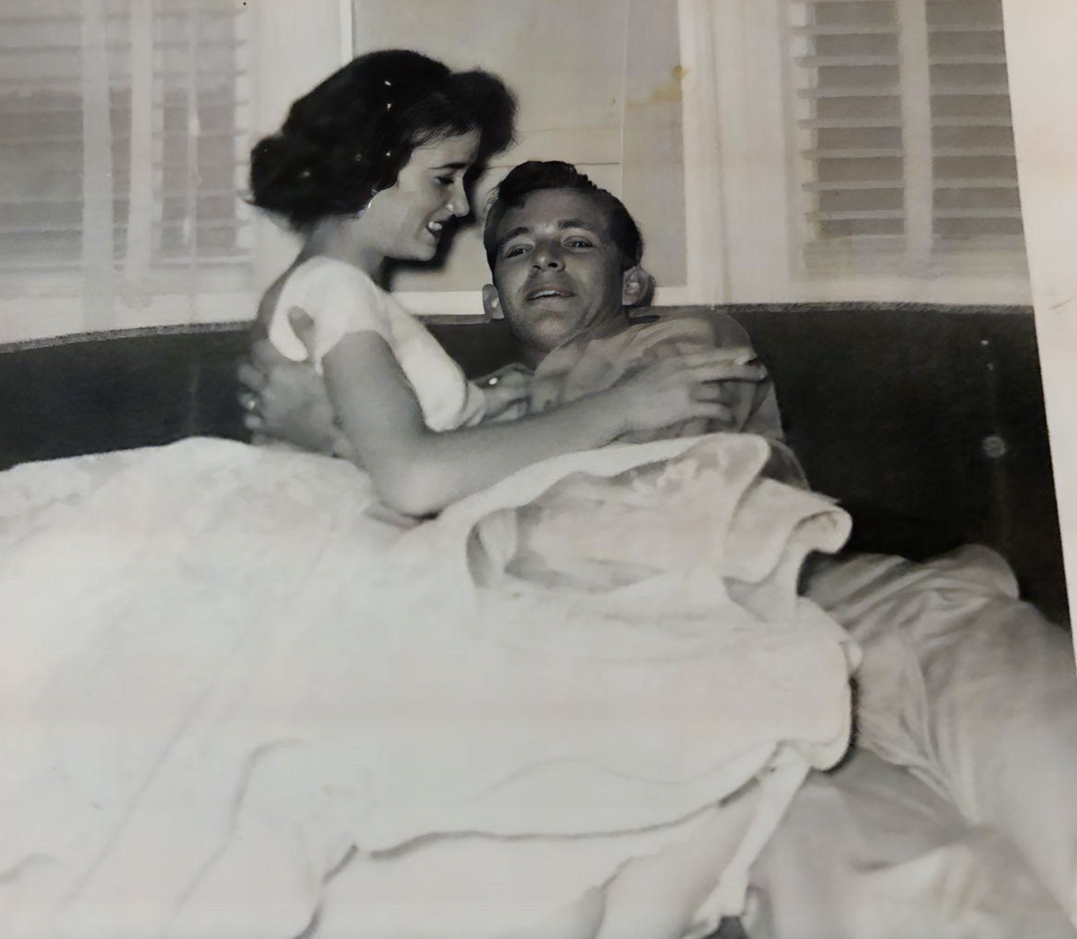 A young couple embracing while sitting on a bed.