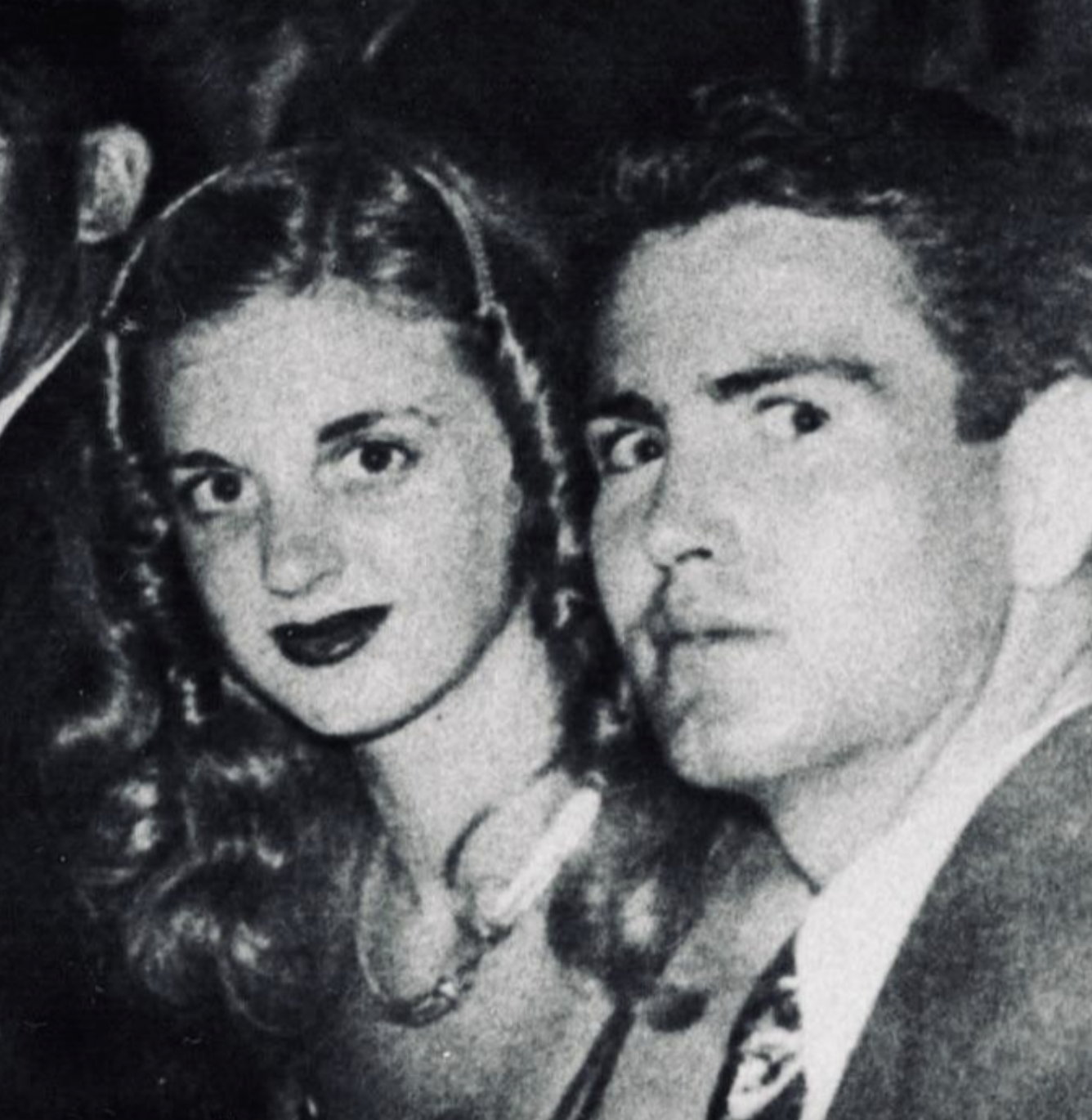 A black-and-white portrait of a young woman and a man posing closely together.