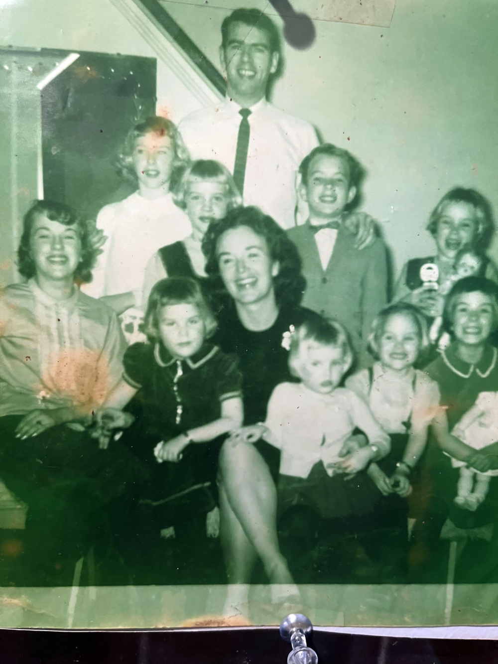 A vintage black-and-white family portrait featuring an adult man and woman surrounded by eight smiling children.