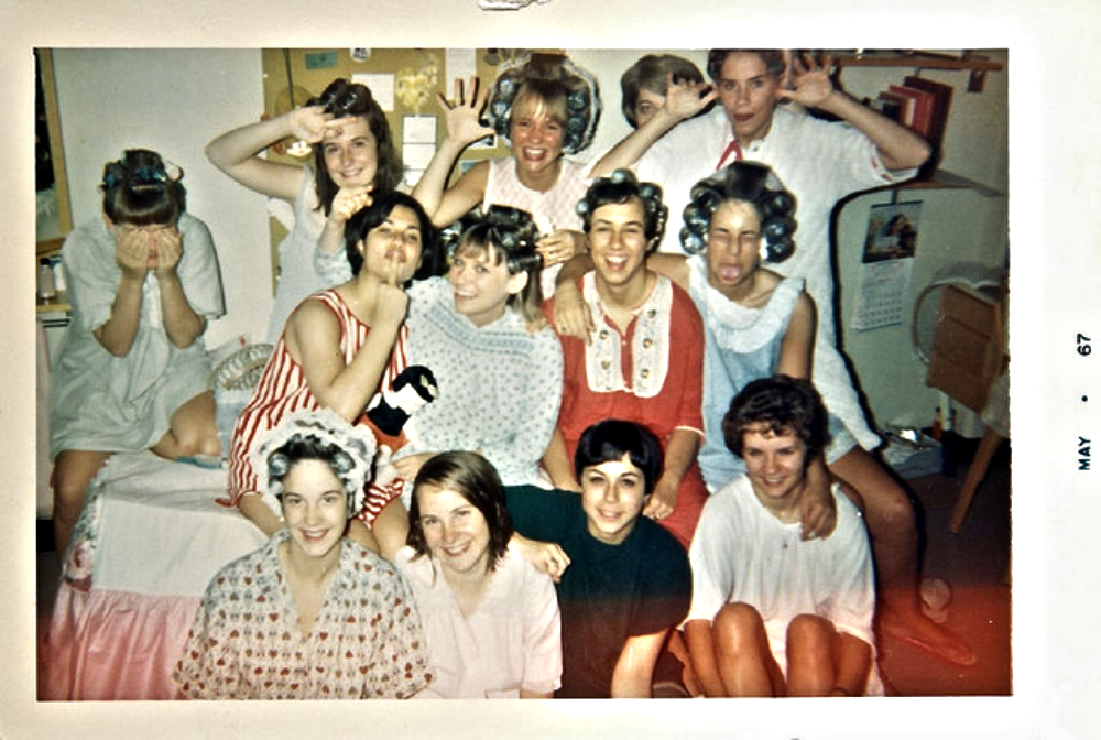 A group of young women at a slumber party, some wearing hair rollers and pajamas, posing for a group photo.