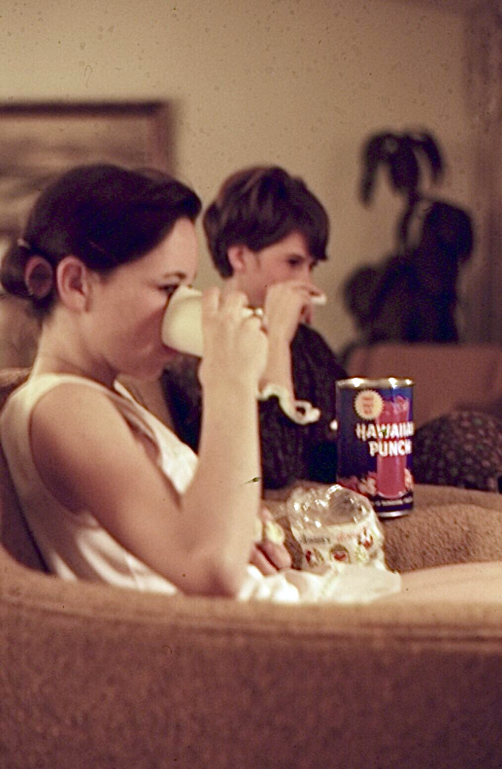 Two people sitting in armchairs drinking from mugs with a can of Hawaiian Punch on the armrest.