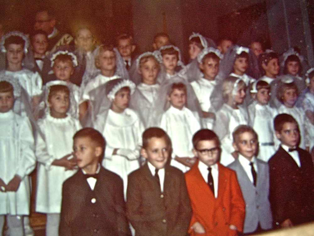 A group of children posing for a formal church portrait, with girls wearing white dresses and veils and boys in suits.
