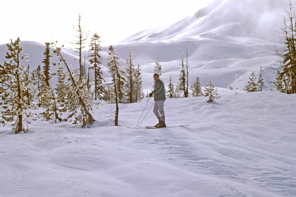 A person cross-country skiing on a snow-covered hillside among scattered trees.