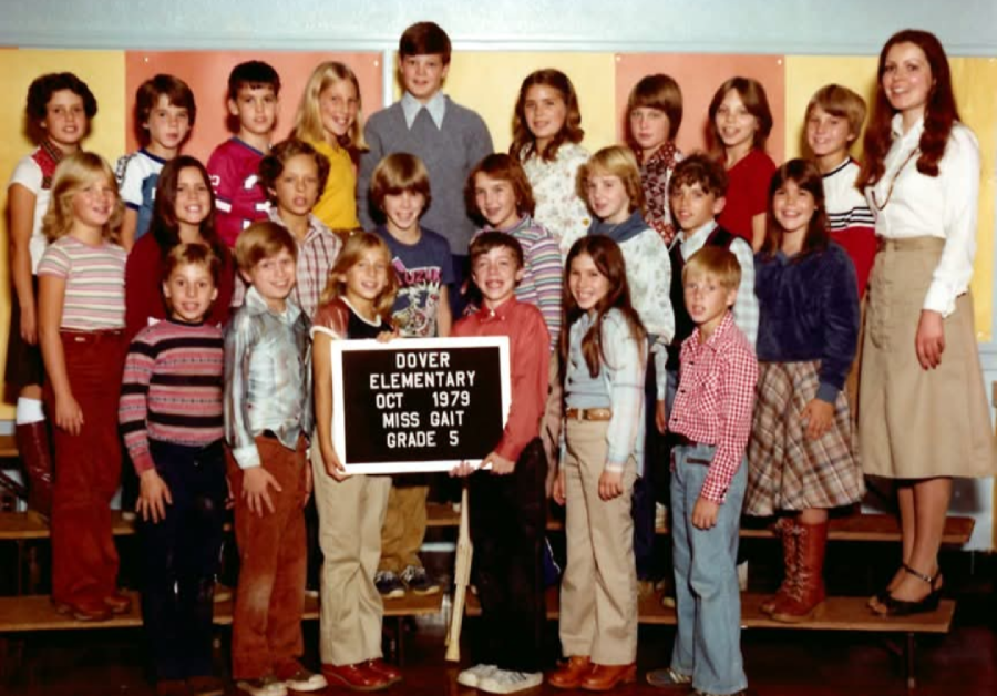 A group of elementary students and their teacher pose for a class photo in 1979. A sign reads “Dover Elementary, Oct 1979, Miss Gait, Grade 5.” The children are smiling and standing on risers.