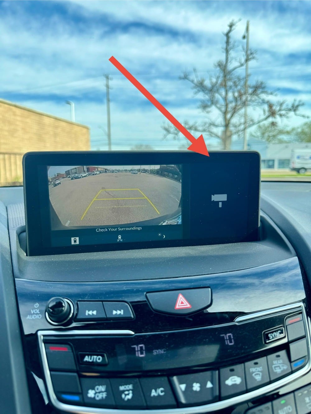 Car infotainment screen displaying a backup camera view with a red arrow pointing to a camera icon on the right side of the display.