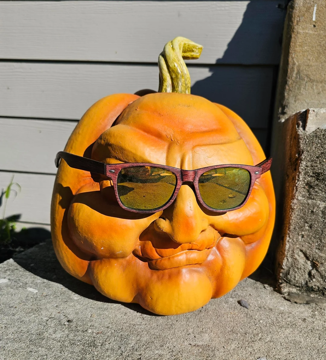 A carved pumpkin with a facial expression wearing wood-framed sunglasses.