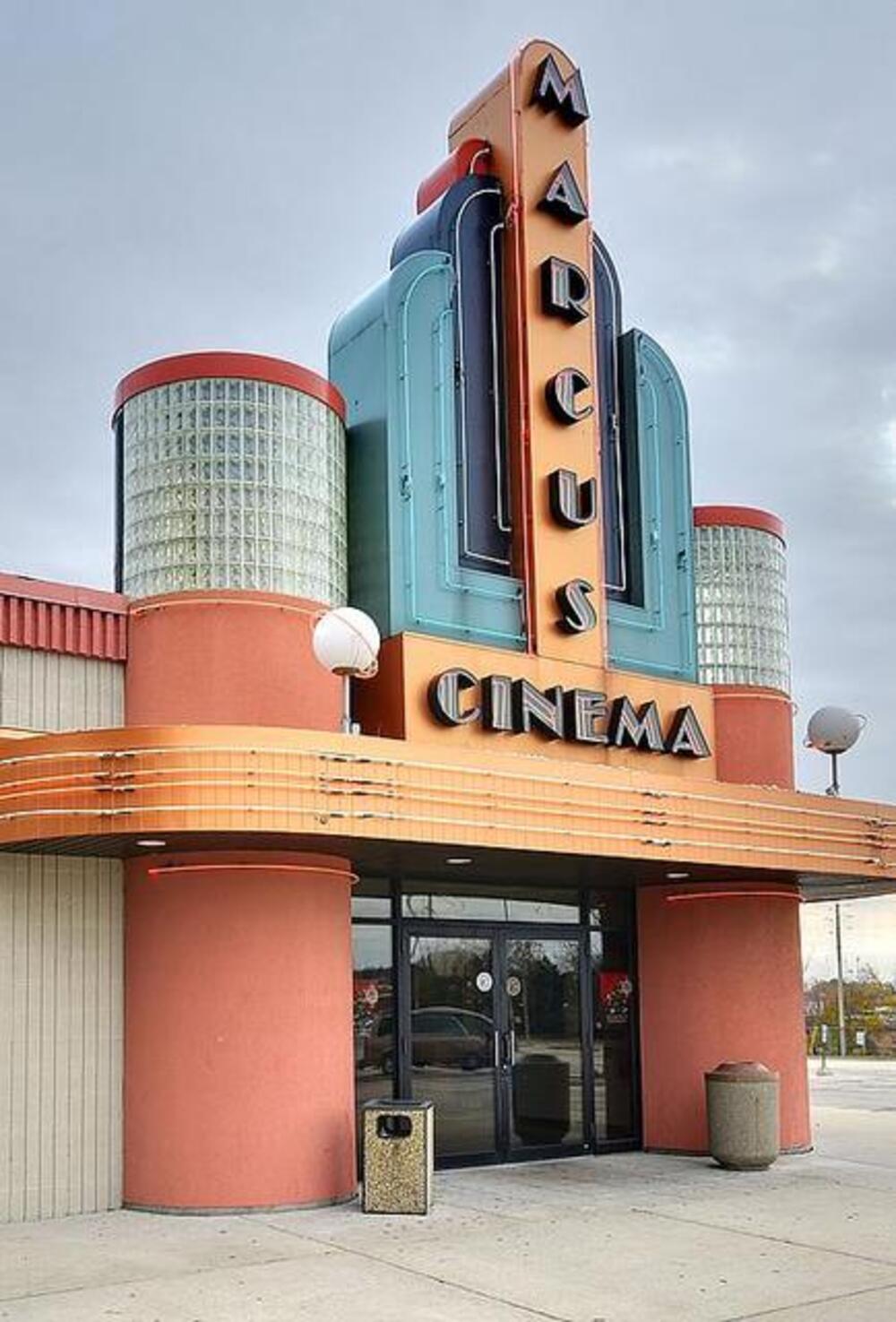 The exterior entrance of a retro-style Marcus Cinema building featuring a tall vertical sign and a curved marquee.
