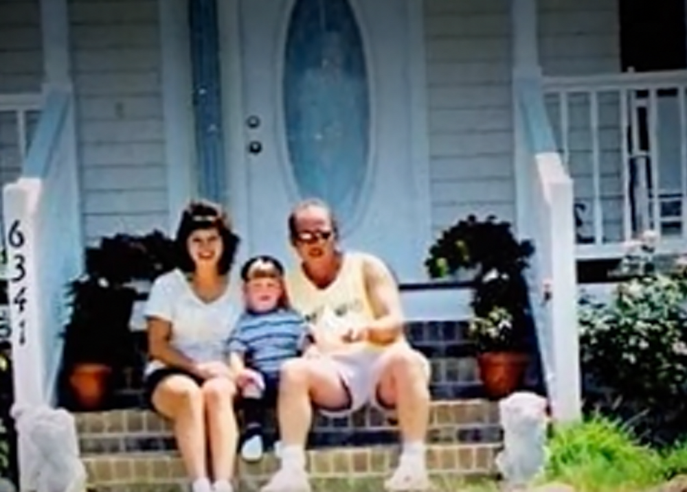 A man, woman, and child sitting together on the front steps of a house.