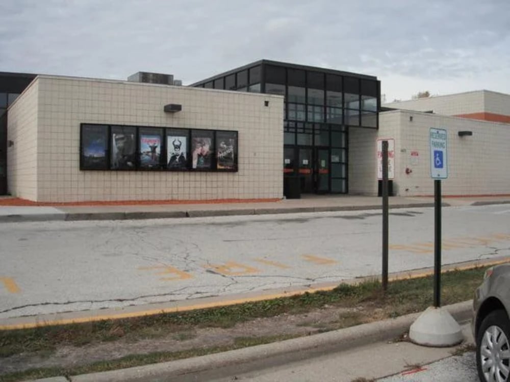 Exterior view of a movie theater with movie posters displayed on the wall near the glass entrance.