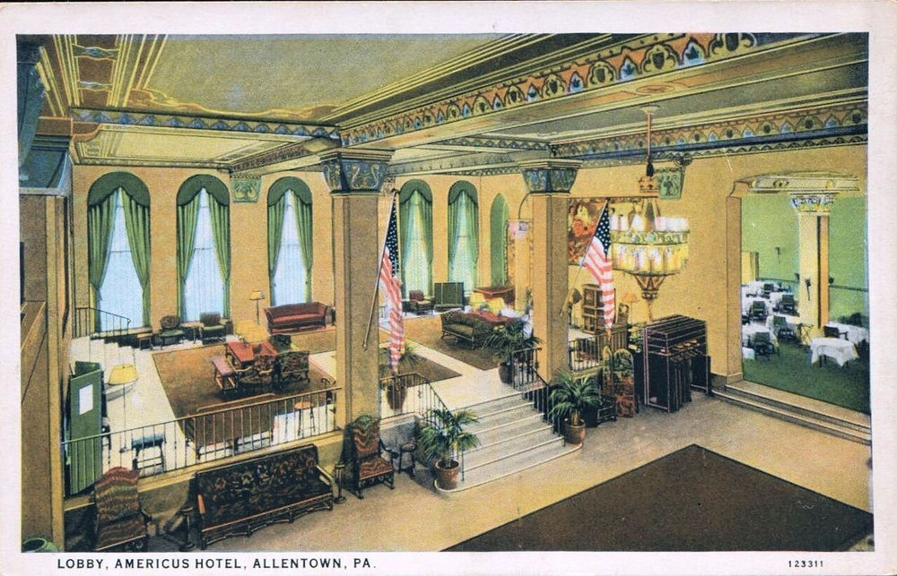 Vintage postcard view of the multileveled lobby of the Americus Hotel in Allentown, Pennsylvania, featuring seating areas, American flags, and decorative columns.