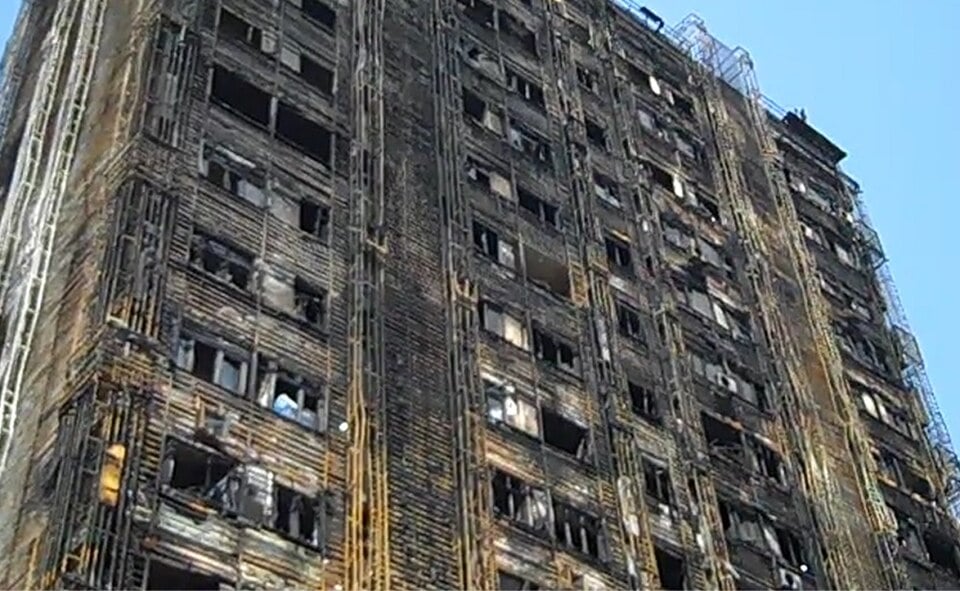 A tall, multi-story apartment building with a blackened exterior from fire damage and broken windows.