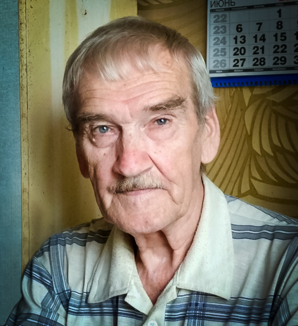 Portrait of an elderly man with gray hair and a mustache wearing a striped collared shirt.