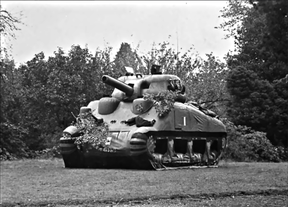 Black and white photograph of an inflatable decoy tank positioned in a field near trees.