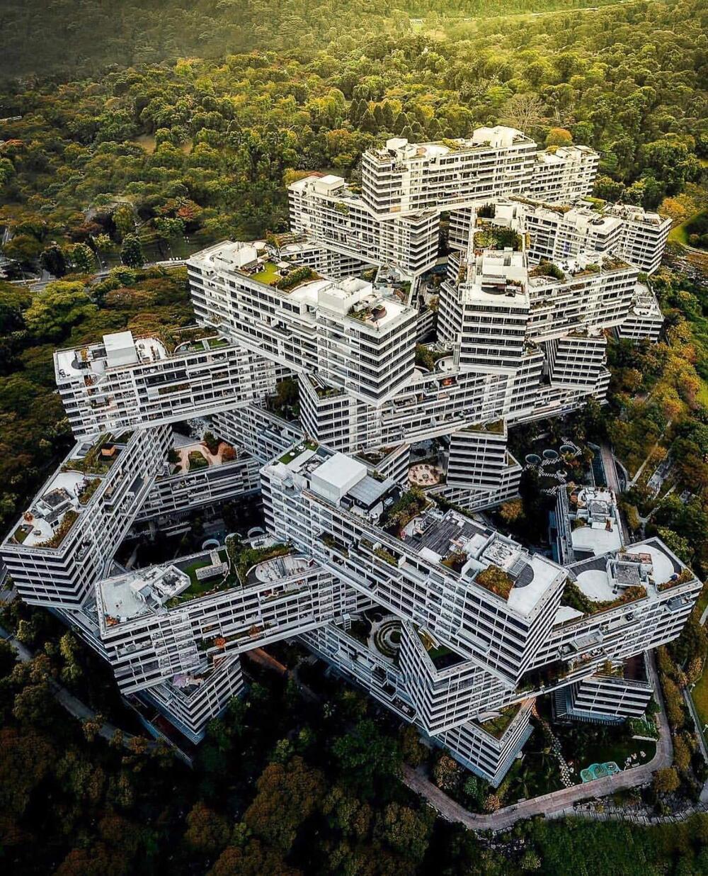 Aerial view of a large residential complex with stacked, interlocking white buildings surrounded by dense forest.