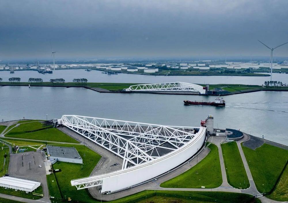 Aerial view of the Maeslantkering storm surge barrier gates in the Nieuwe Waterweg channel with a cargo ship passing through.