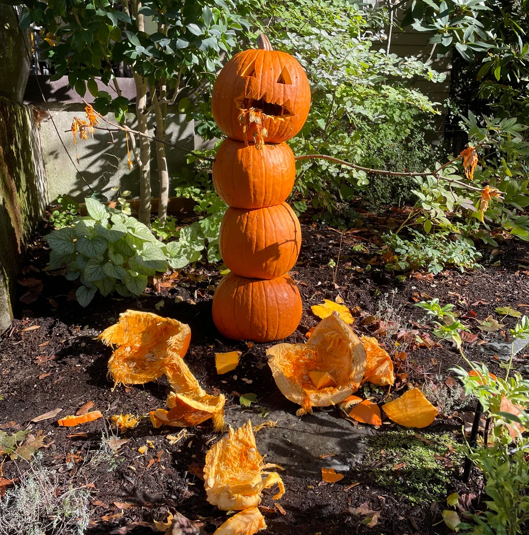 A stack of four pumpkins, with the top one carved into a jack-o’-lantern appearing to vomit pumpkin guts onto the ground.