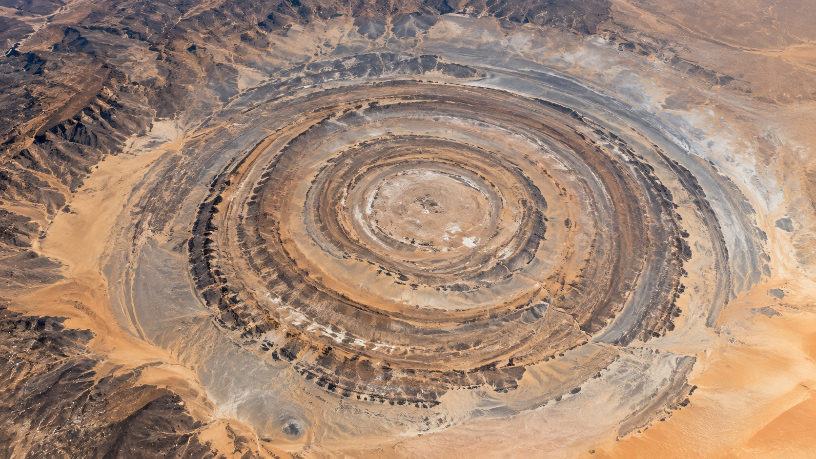 Aerial view of the Richat Structure, a large, circular geological formation in the desert featuring prominent concentric rings of rock.