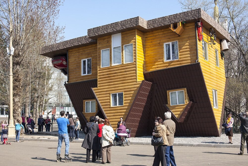 An upside-down wooden house attraction with people standing in the foreground.
