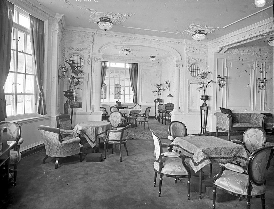 Interior of a formal lounge or dining room featuring ornate white walls, decorative ceilings, and several small tables with chairs.