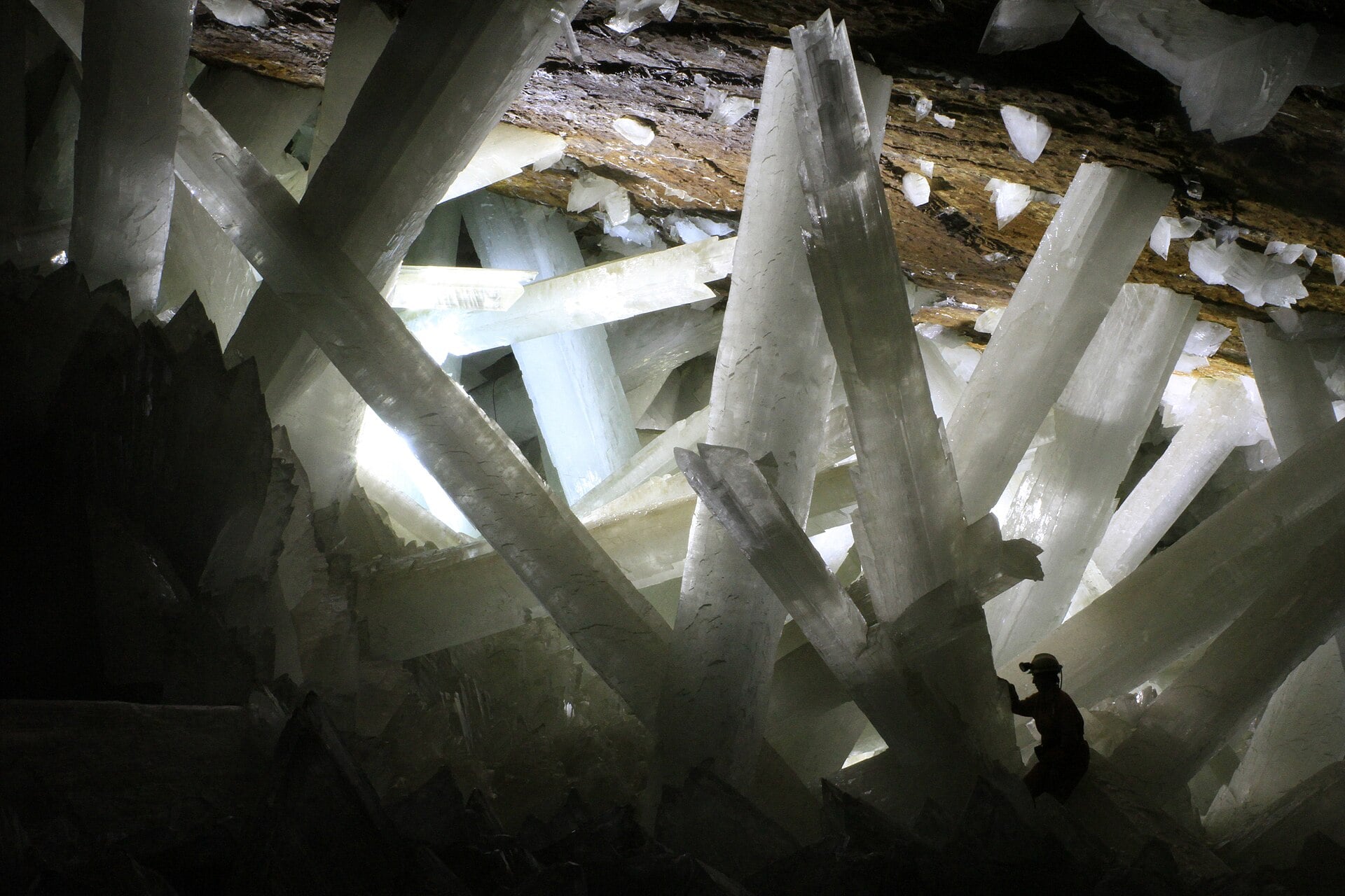 A person in a hard hat stands among massive translucent selenite crystals in a cave.