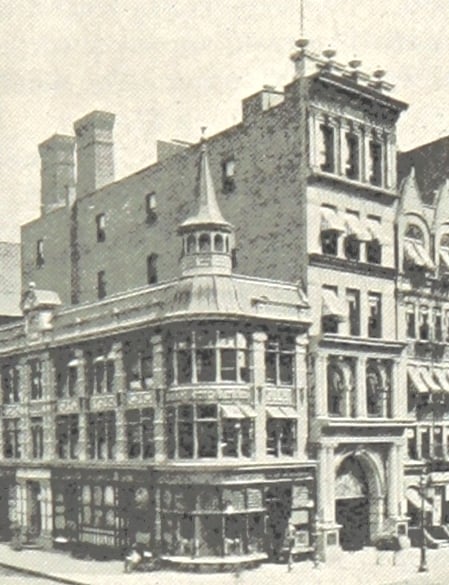 A multi-story commercial building on a street corner featuring a turreted roof section and large arched windows.