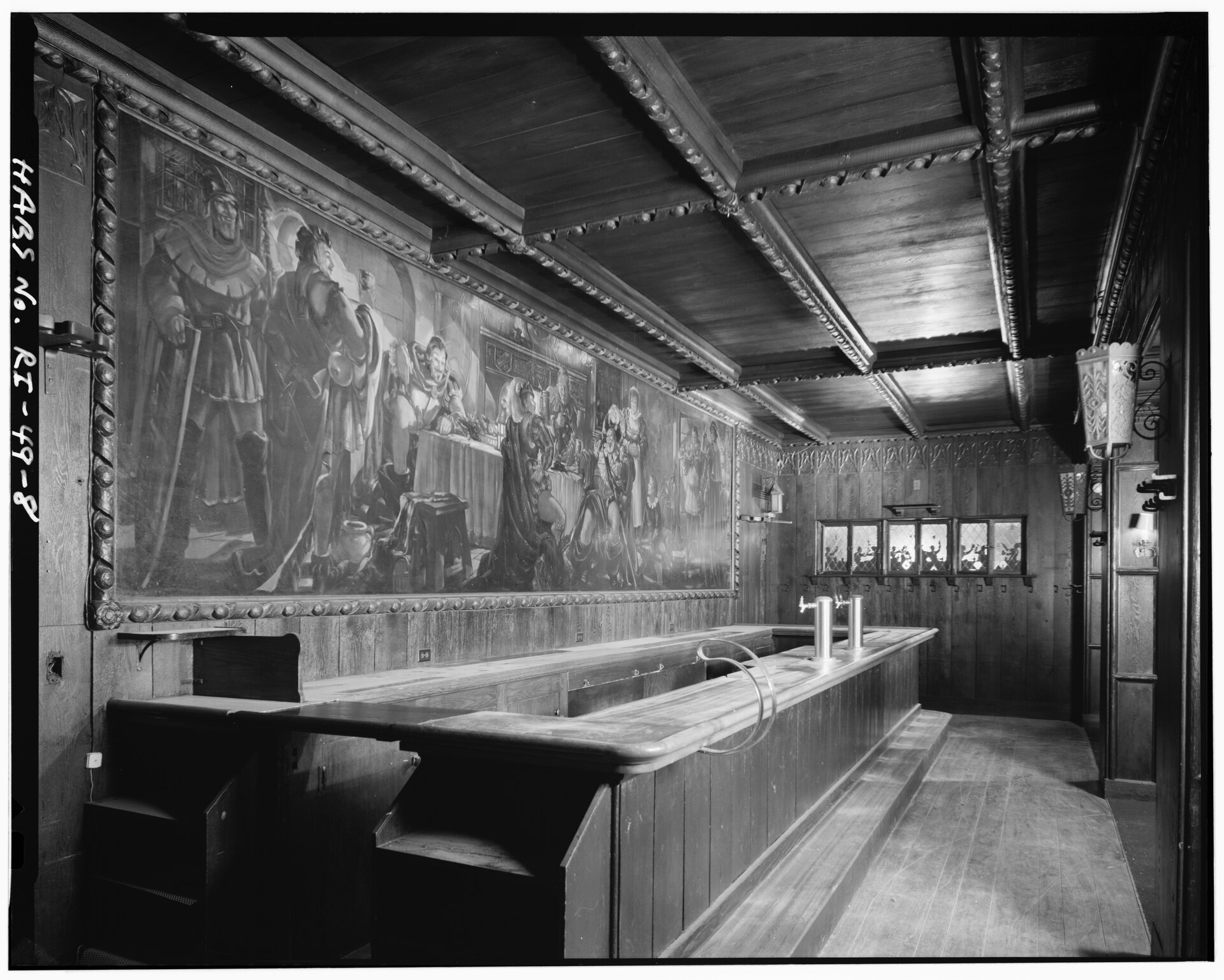 A wood-paneled tavern interior featuring a long bar and a large mural depicting medieval figures dining.