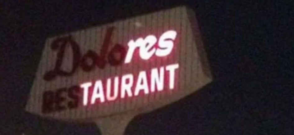 A lit roadside sign for Dolores Restaurant against a dark background.