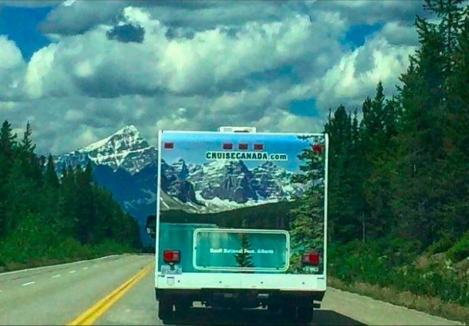 A CruiseCanada rental RV driving on a mountain highway with a snowy peak in the background.