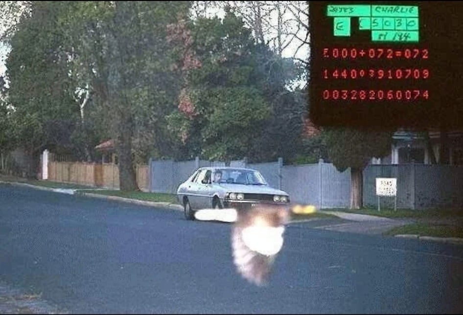 A security camera shot of a car driving on a suburban street with a bright, blurred light streak in the foreground and data readouts in the corner.