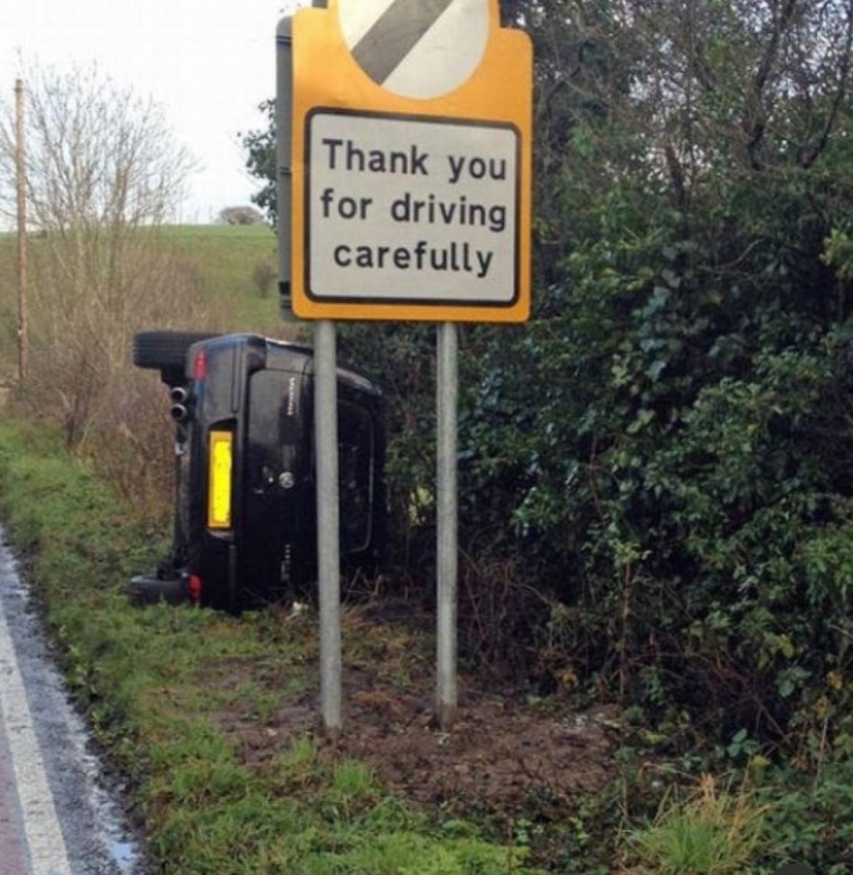 A car crashed into a ditch behind a road sign that reads, “Thank you for driving carefully.”