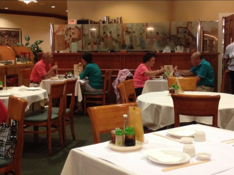 Patrons dining at tables in a restaurant decorated with a glass partition featuring Asian-style artwork.