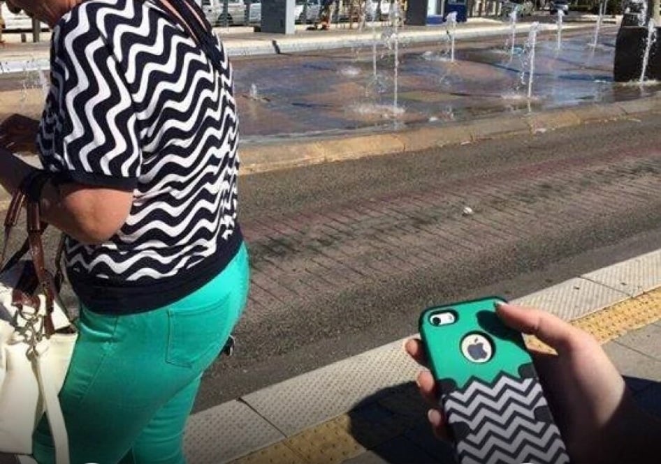 A person holding a green and black chevron-patterned phone case that matches the shirt of a woman walking in front of them.