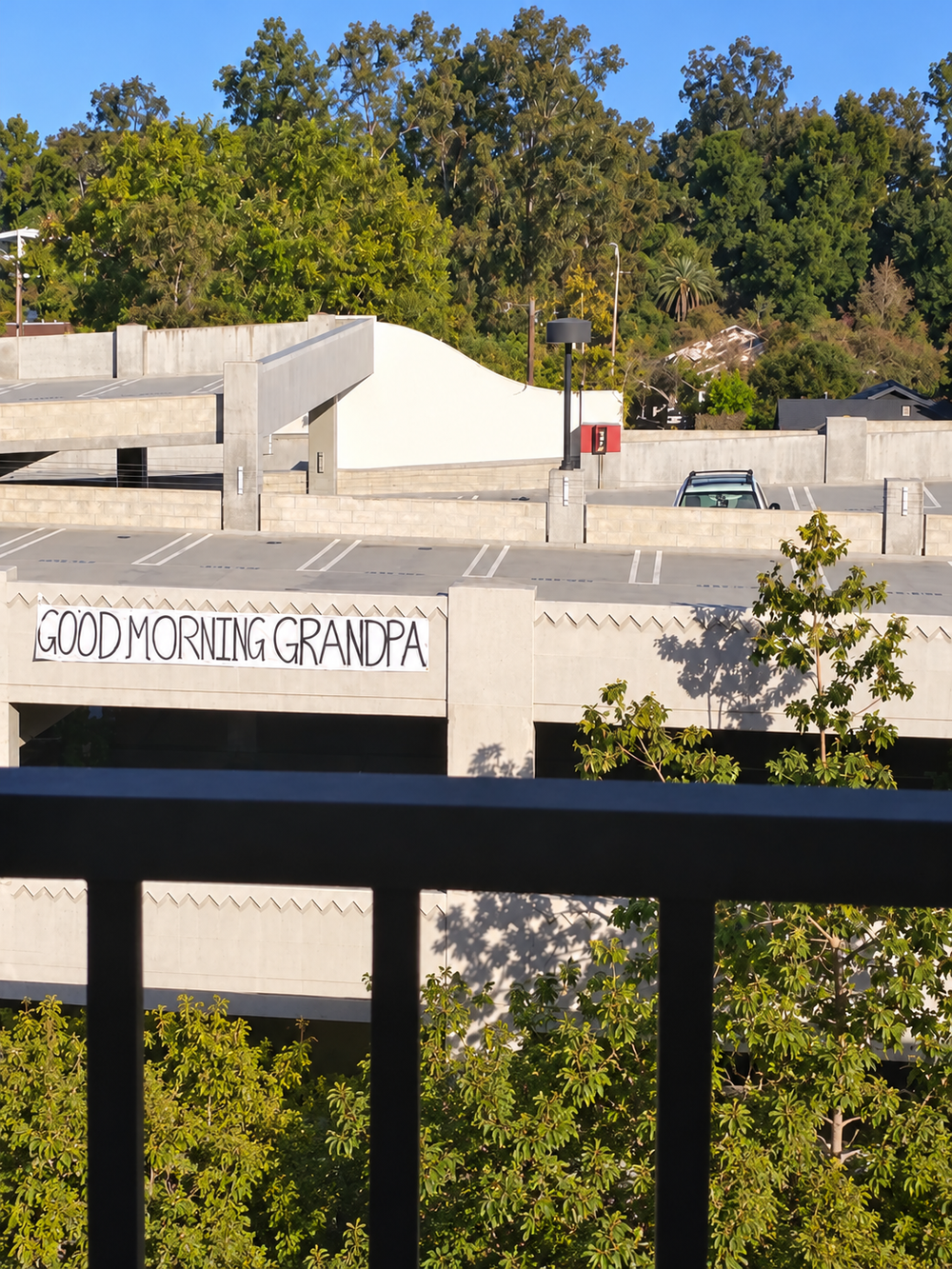 A banner reading “GOOD MORNING GRANDPA” hung on the side of a concrete parking garage.