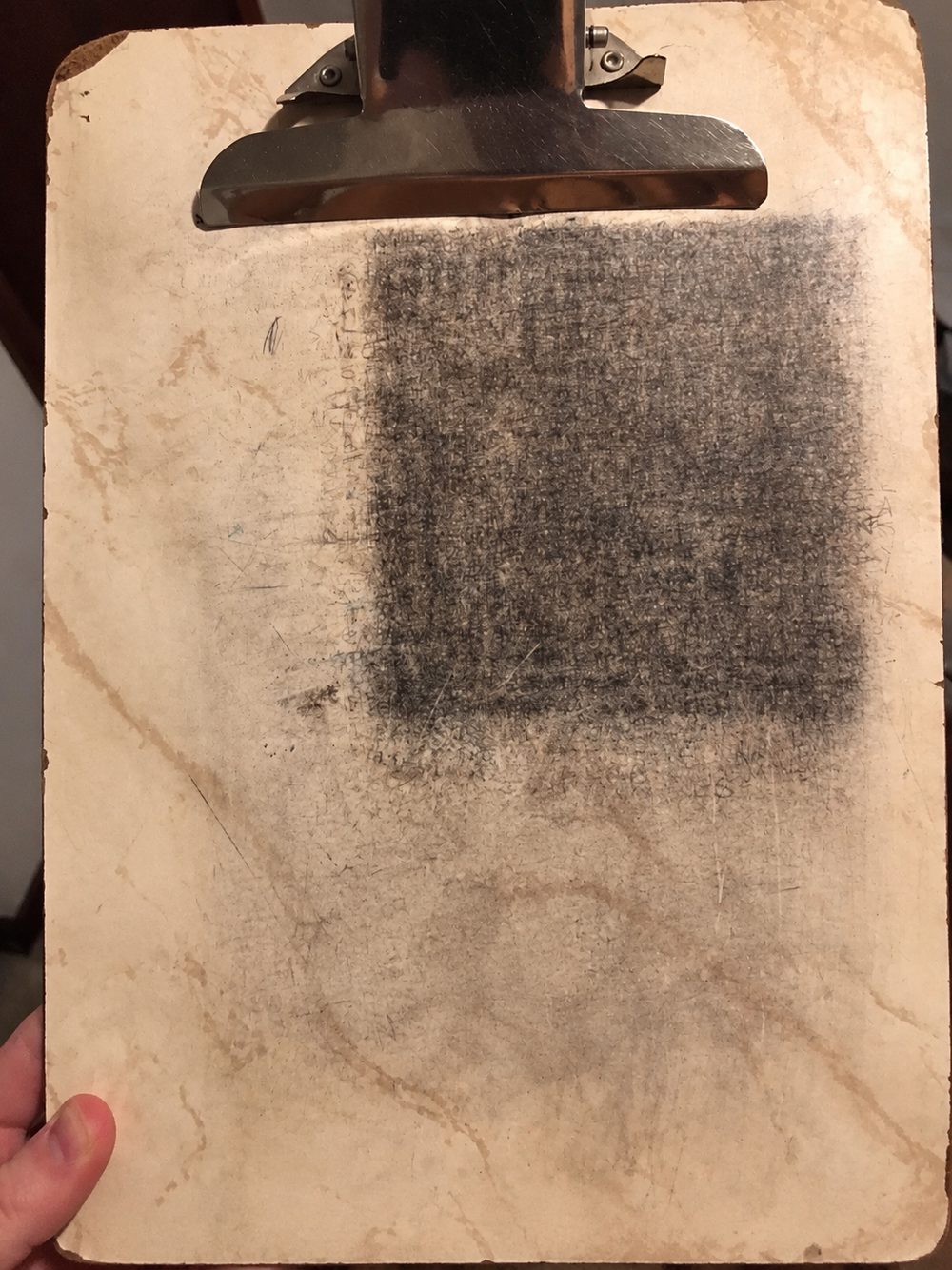 A clipboard with a large dark rectangle of writing impressions and scratches.